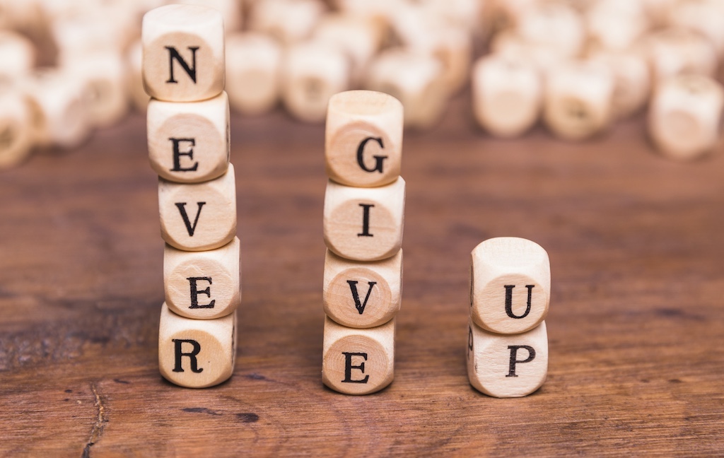 Aufeinander gestapelte Würfel mit Buchstaben darauf. Gelesen ergibt das Never give up